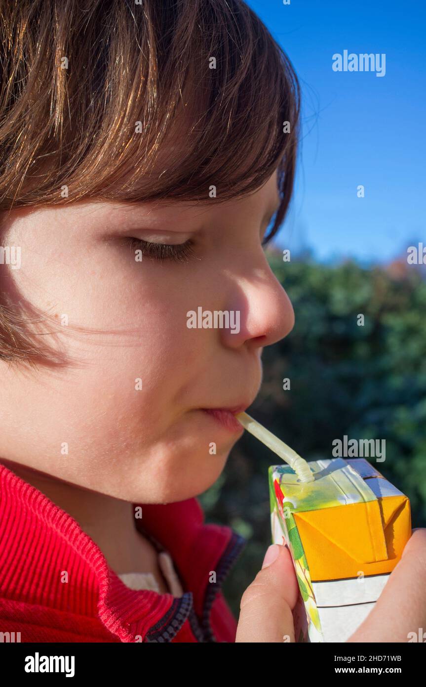 Child boy drinking sweetened juice fruit juice from brick. Fruit juice for children concept. Stock Photo