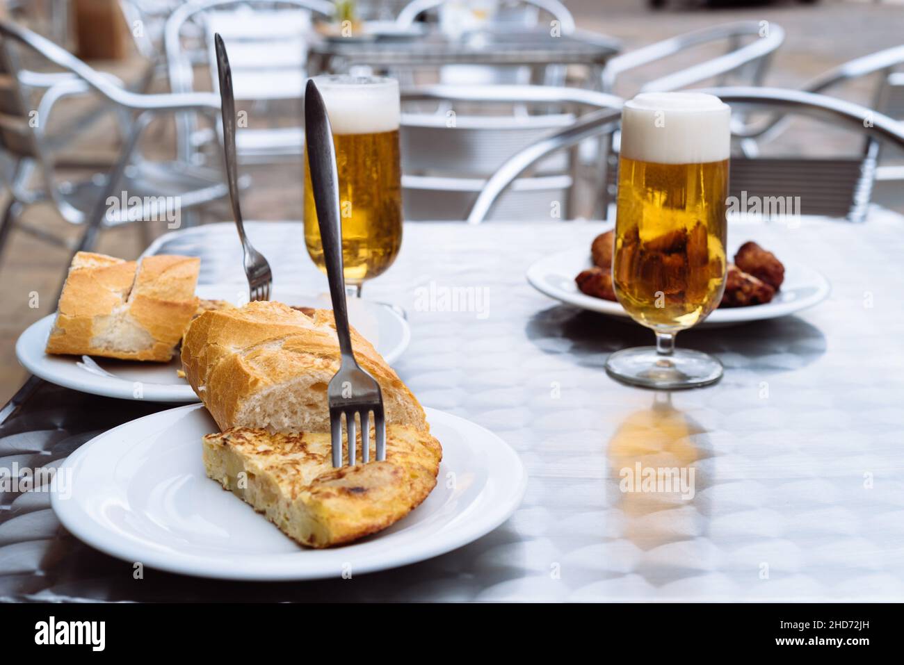 Ice cold beers pouring into glasses on table of terrace with tapas os spanish omelette and chicken wings. Space for copy. Stock Photo