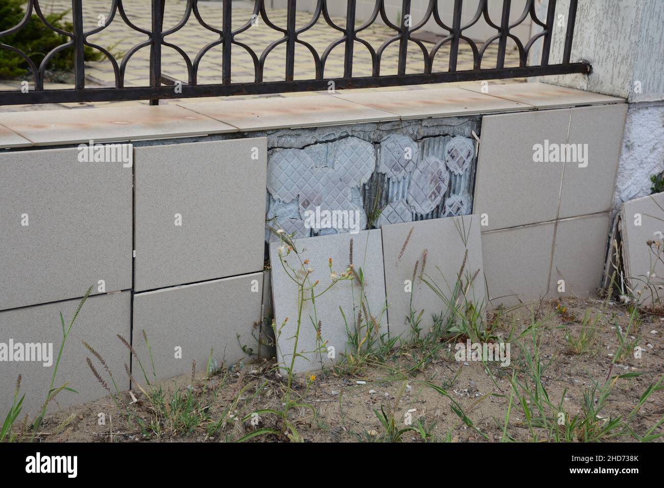 Ceramic tiles fall off concrete fence footing outdoors. A close-up of a wrought iron fence with concrete tiled footing with tiles that fell off. Stock Photo