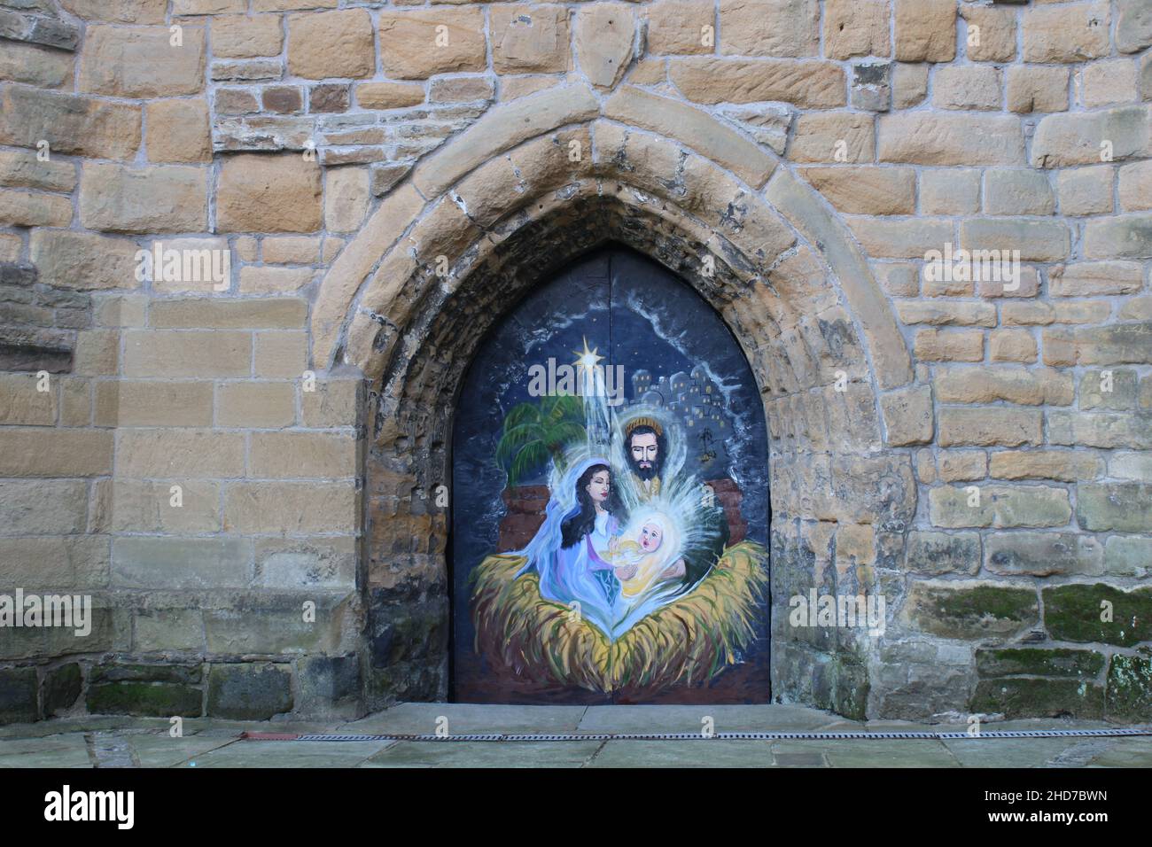 Church stone archway with weathered carvings with Mary, Joseph and baby Jesus mural on the doors at St Thomas the Martyr Church, Upholland, Lancashire Stock Photo