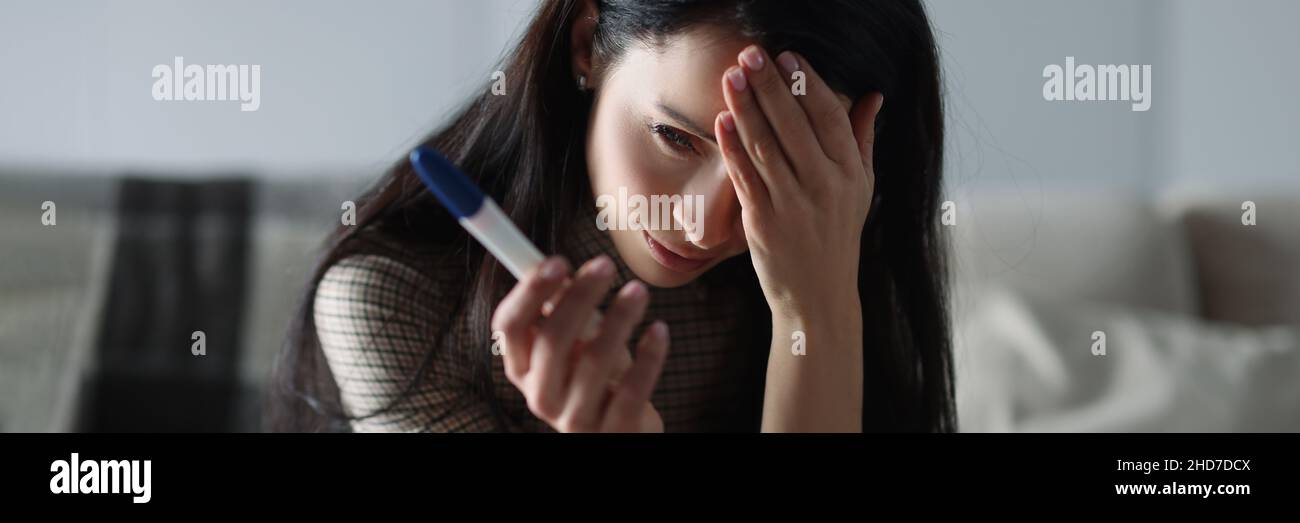 Upset woman holding pregnancy test while sitting on couch Stock Photo