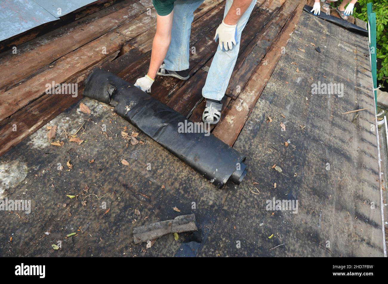 Old roof repair and renovation. A man is removing old bitumen or