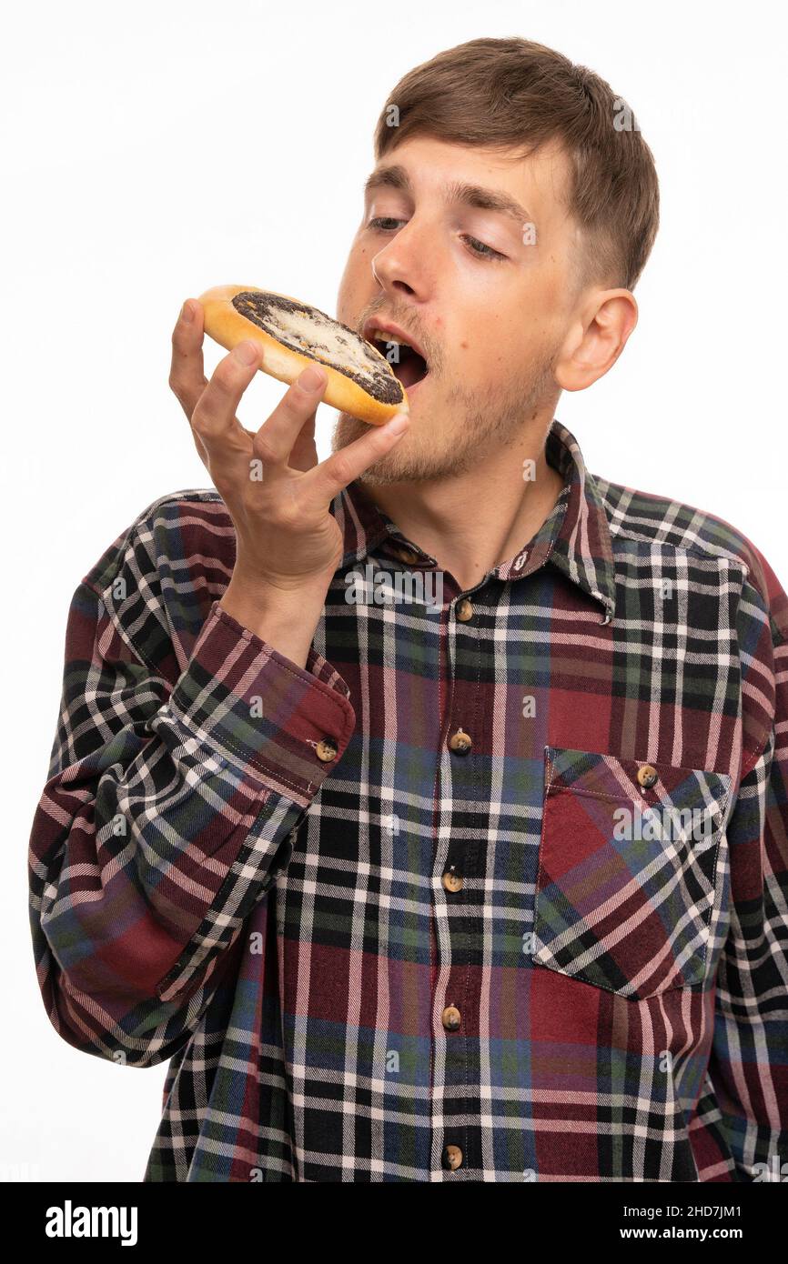 Young handsome tall slim white man with brown hair biting into kolach in flannel shirt isolated on white background Stock Photo