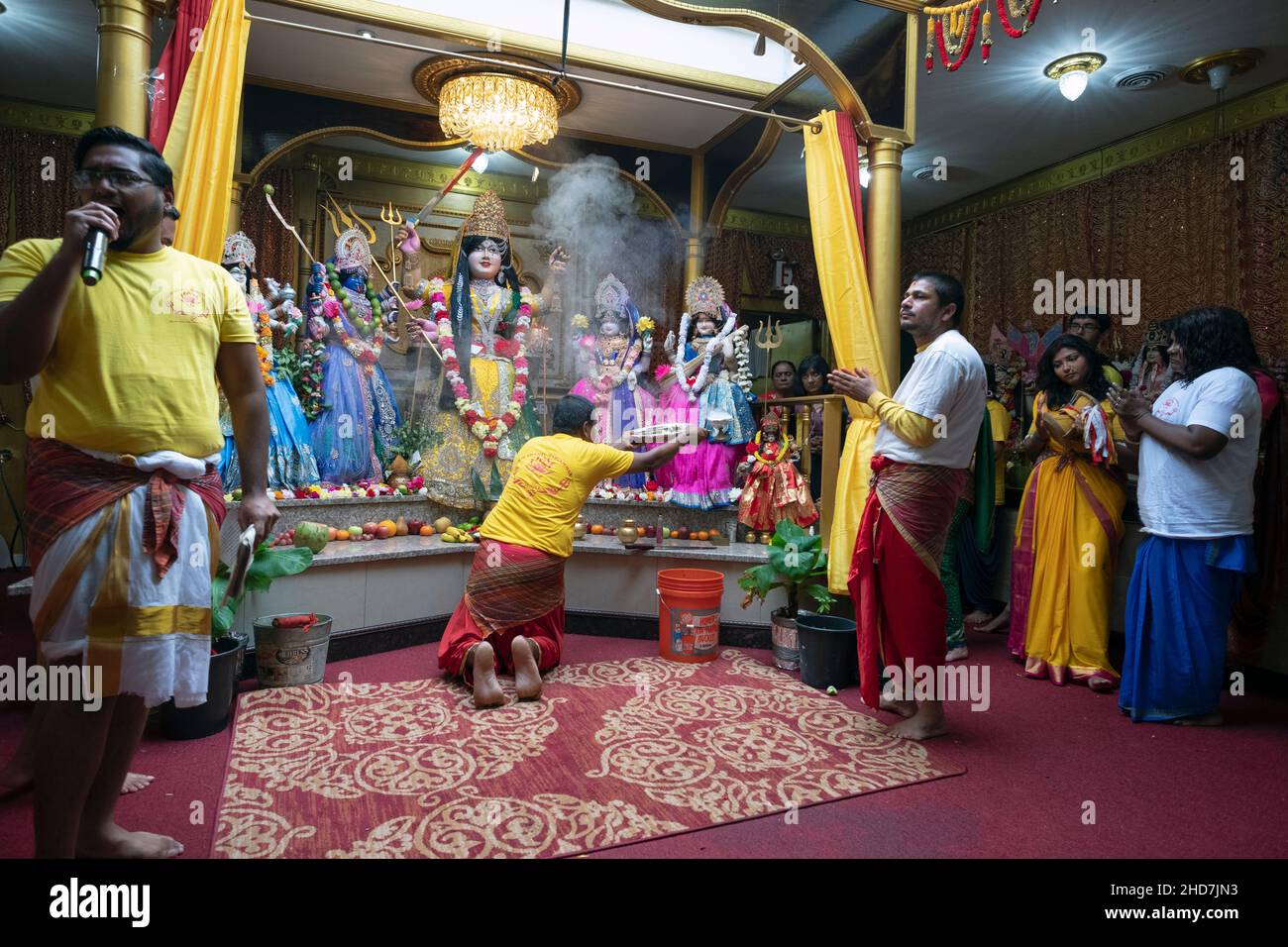 In a Hindu temple a worshipper performs the arti ritual of waving flames in front of statues of deities Stock Photo