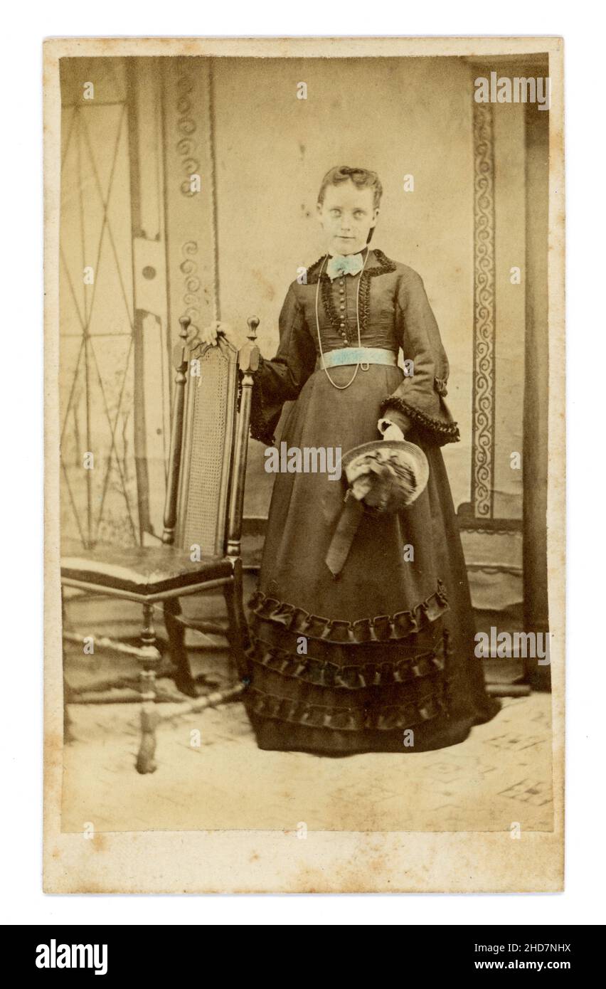 Original Victorian CDV studio portrait of young woman or most probably a teenage girl holding a bonnet, blue hand coloured tint added to waistband and collar, she looks sickly, slightly spooky photograph. Circa 1860's, U.K. Stock Photo