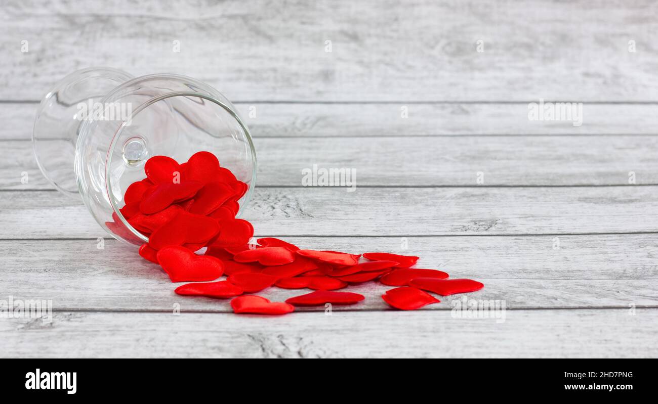 crystal wine glass filled with silk hearts on a light, wooden background. Valentine's Day holiday concept. Stock Photo