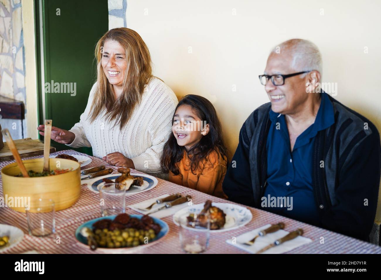 Happy latin grandparents having fun eating with her granddaughter at home - Focus on grandmother face Stock Photo
