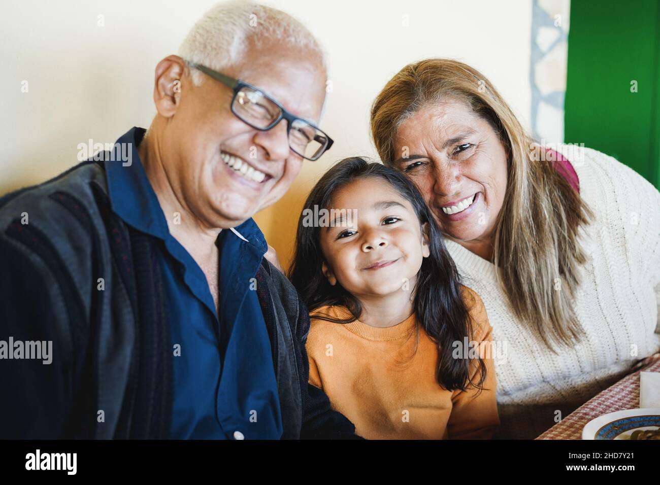 Happy latin child having fun eating with her grandparents at home - Focus on girl face Stock Photo