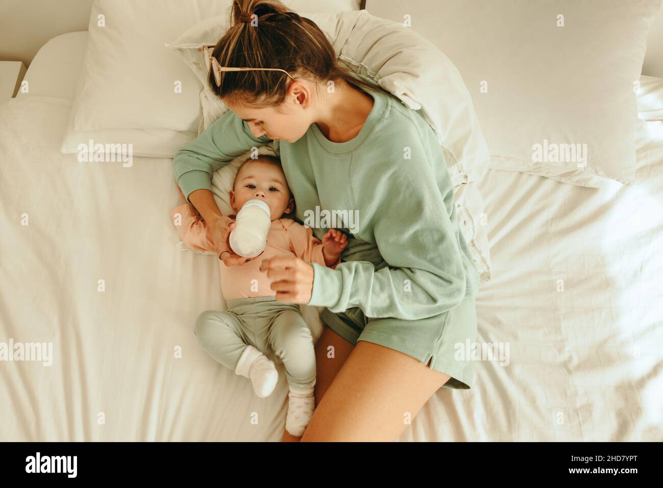 Overhead view of a loving mother feeding her newborn baby. High angle view of a new mom giving her baby formula milk while lying on the bed. Single mo Stock Photo