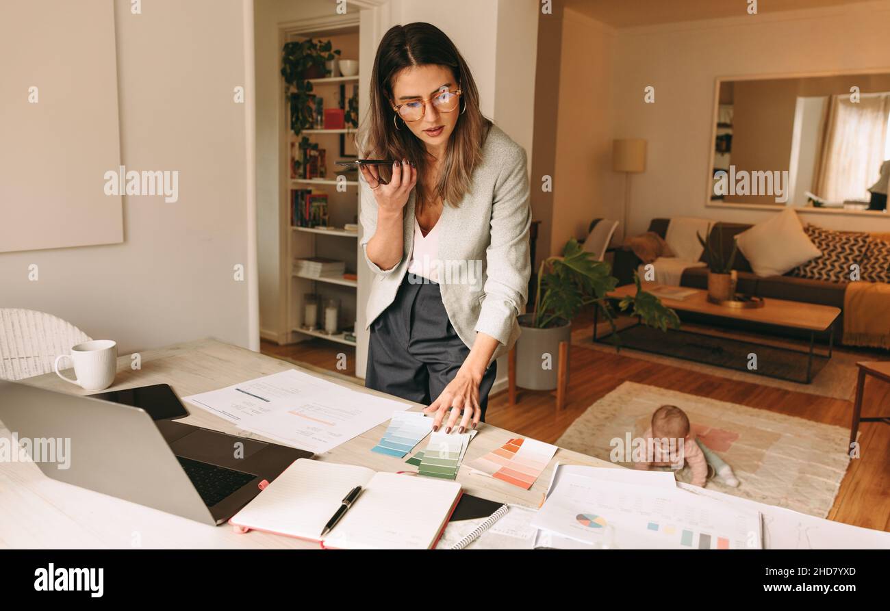 Working mom speaking on the phone in her home office. Female interior designer looking at colour palettes during a phone call. Single mother planning Stock Photo