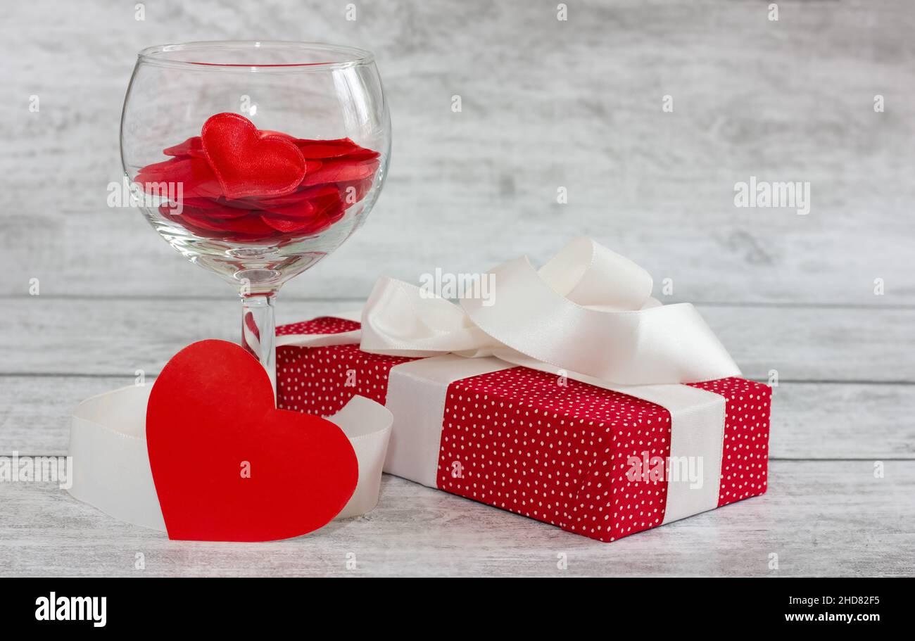 glass with hearts and a red gift box with a white bow on a wooden background. holiday concept Stock Photo