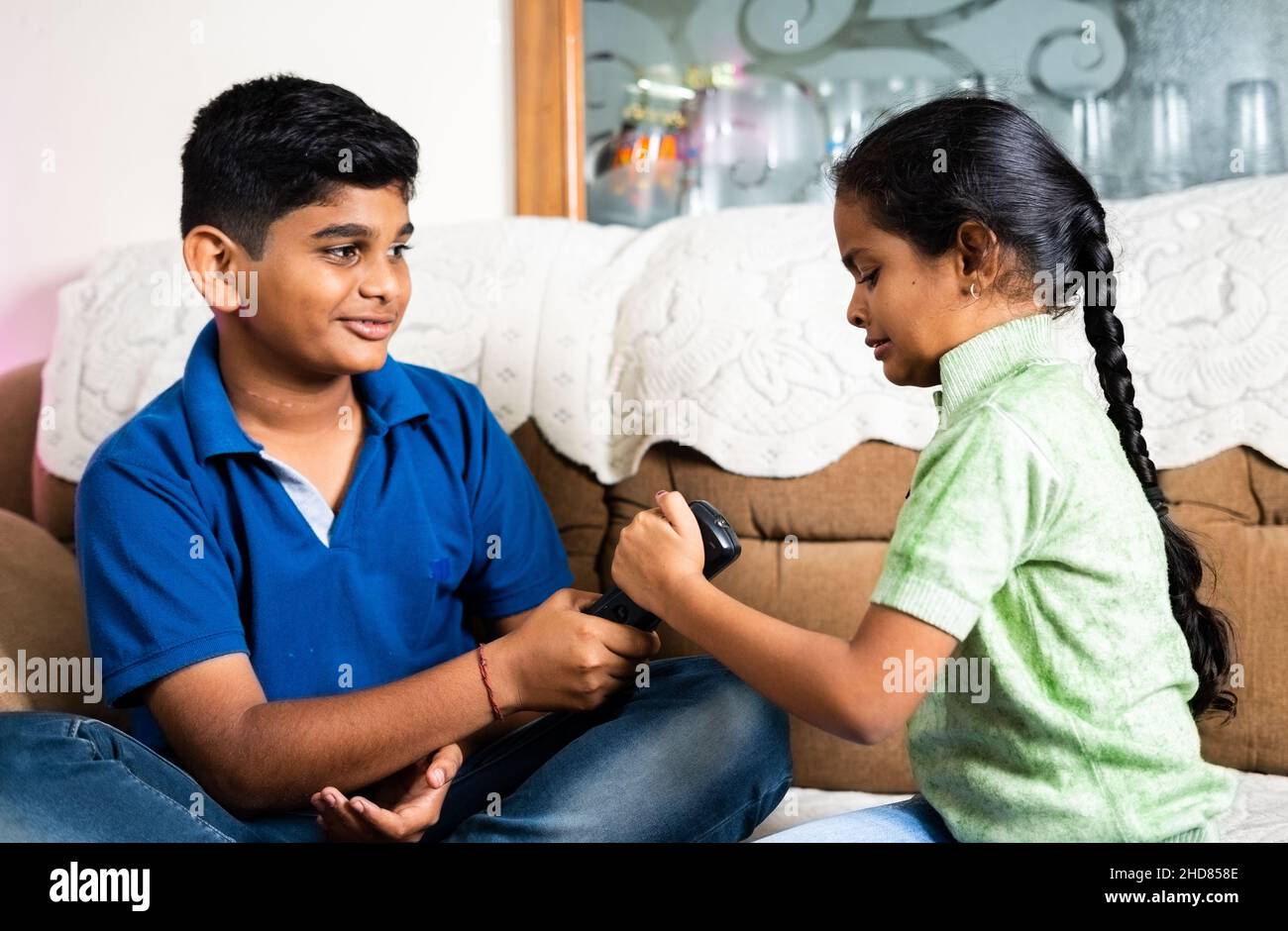 Focus on girl, Kids fighting for remote control while watching television or tv at home - concept of sibling disagreement, quarrel and childhood Stock Photo