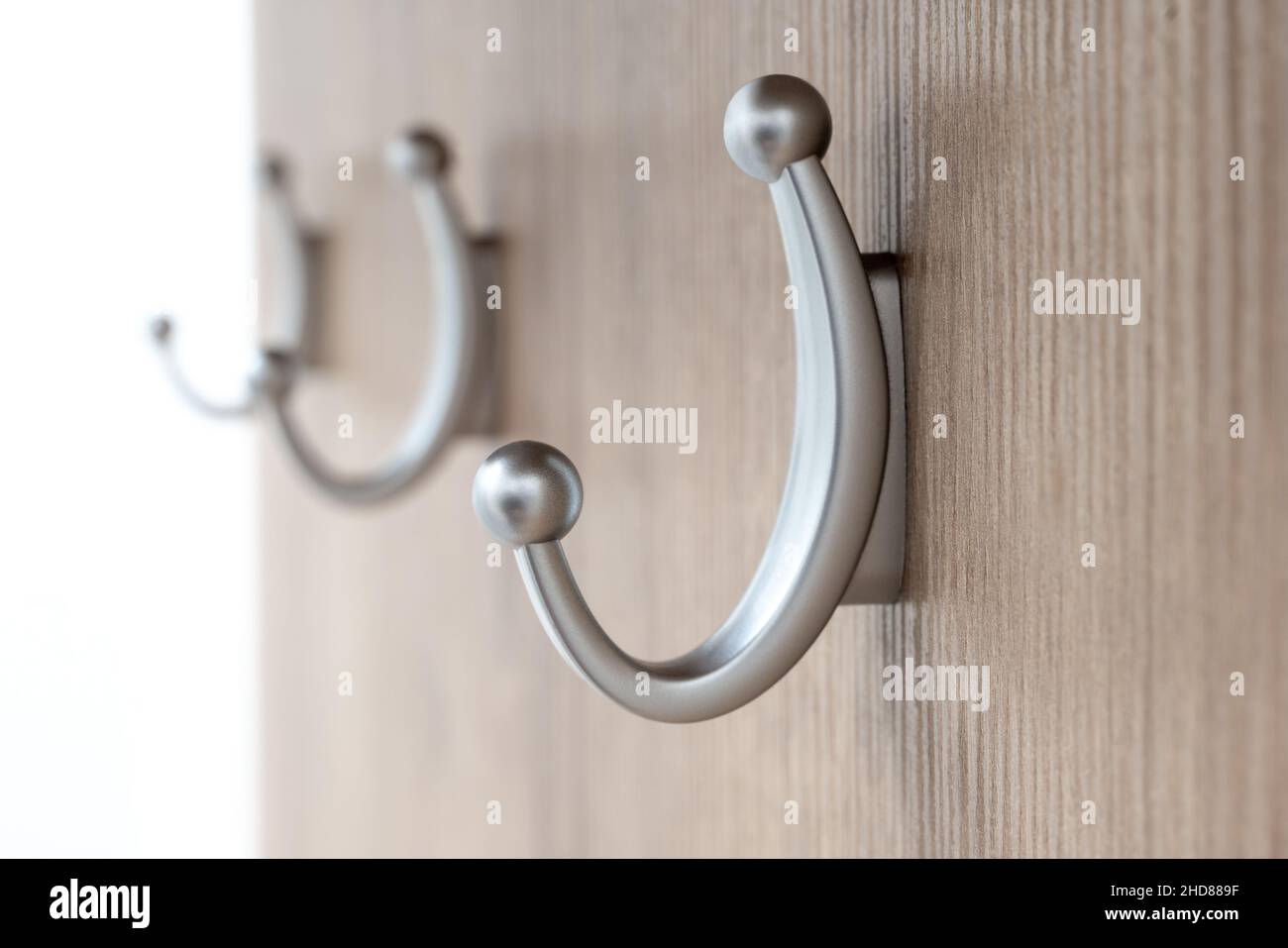 Three medium sized, silver colored coat hangers attached to a wooden board with focus on the first one. Home door hall equipment. Coat hangers by Stock Photo