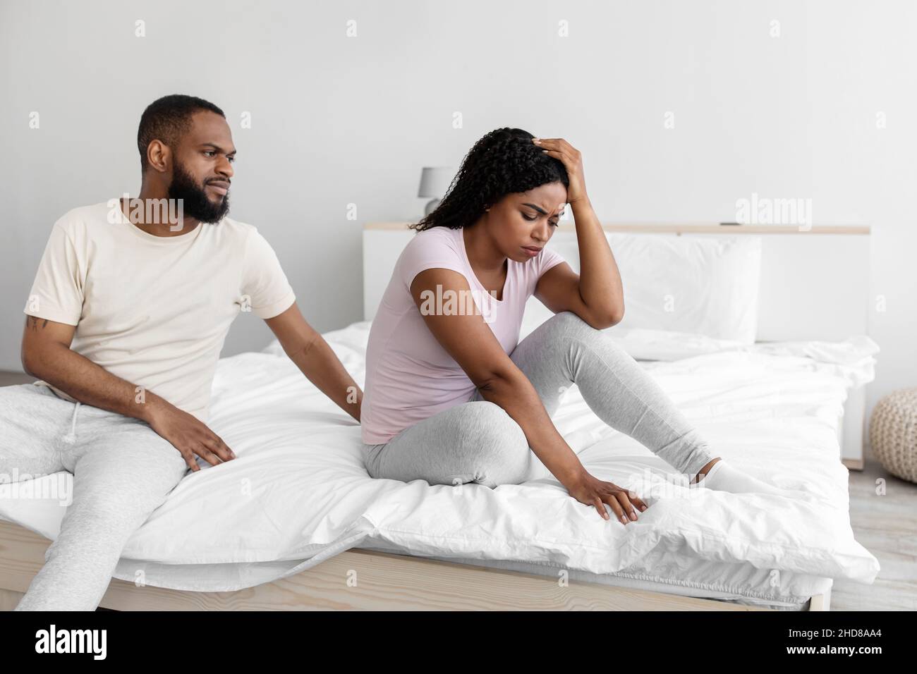 Serious young black man calm to sad desperate depressed wife, sit on bed in bedroom interior Stock Photo