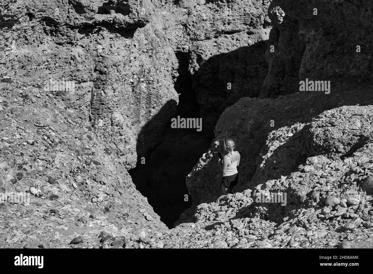 Unrecognizable female tourist looking into deep dark cave and taking photos in Namibia Stock Photo