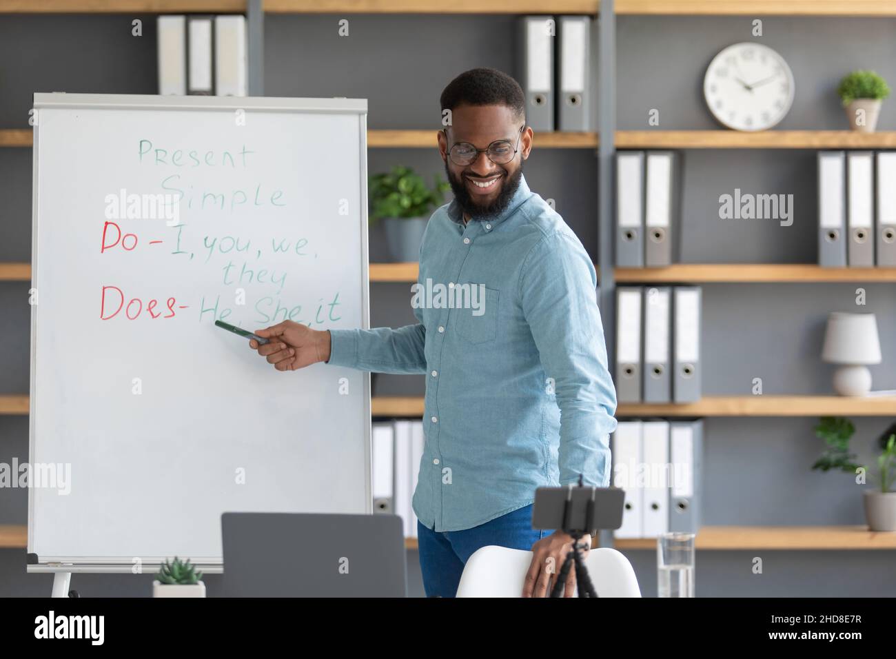Glad friendly millennial african american male blogger teacher points to English rules on blackboard Stock Photo