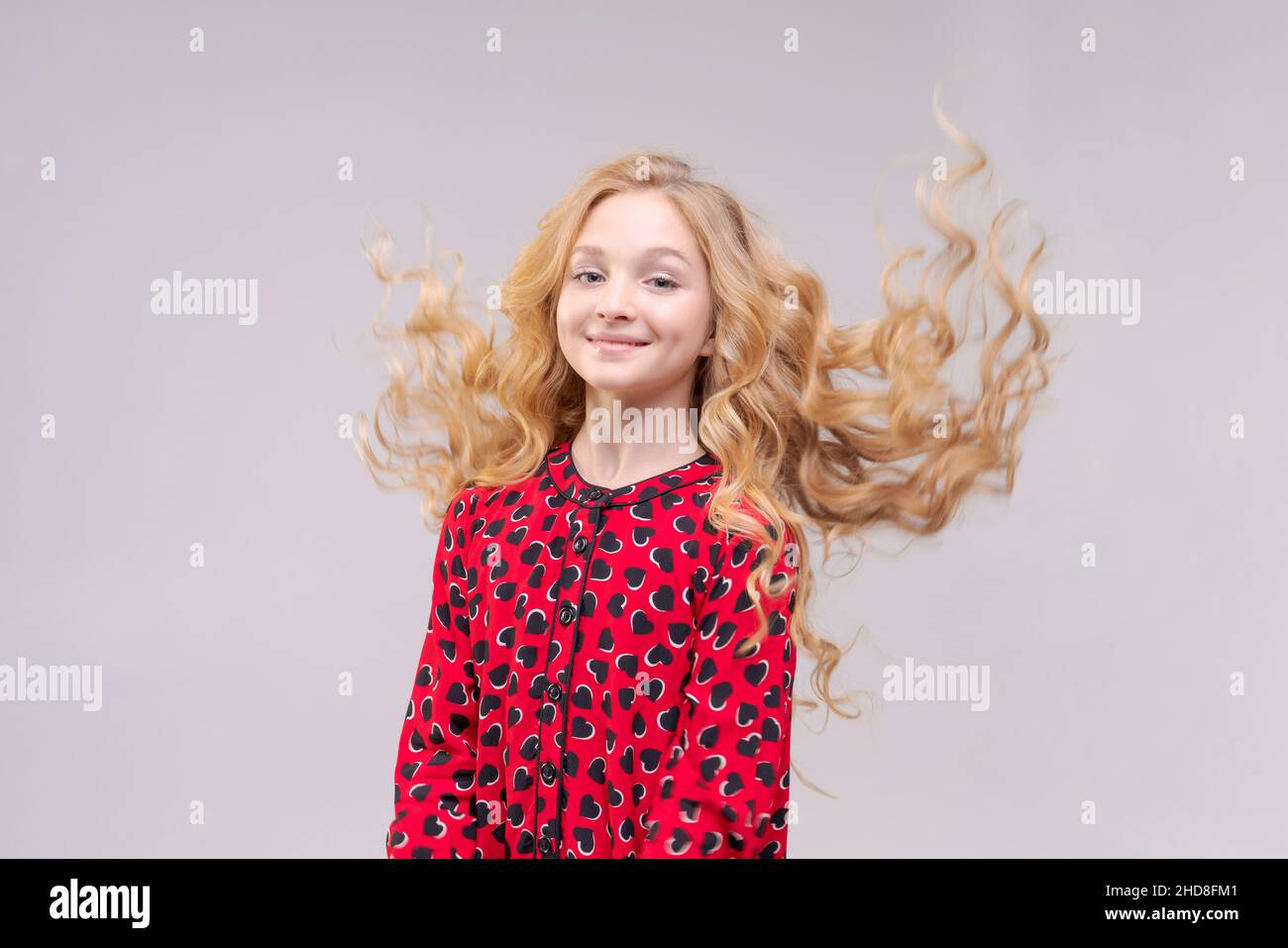 A beautiful cheerful girl in red dress with flying long wavy hair on ...