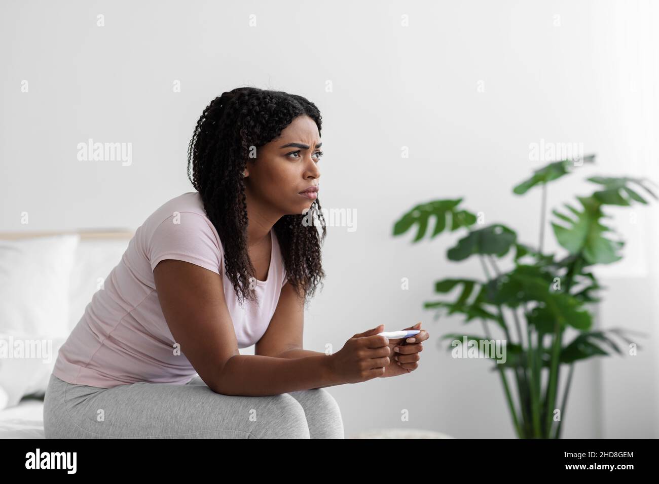 Frustrated sad young black woman sitting on bed and looking at negative pregnancy test have female health problems Stock Photo