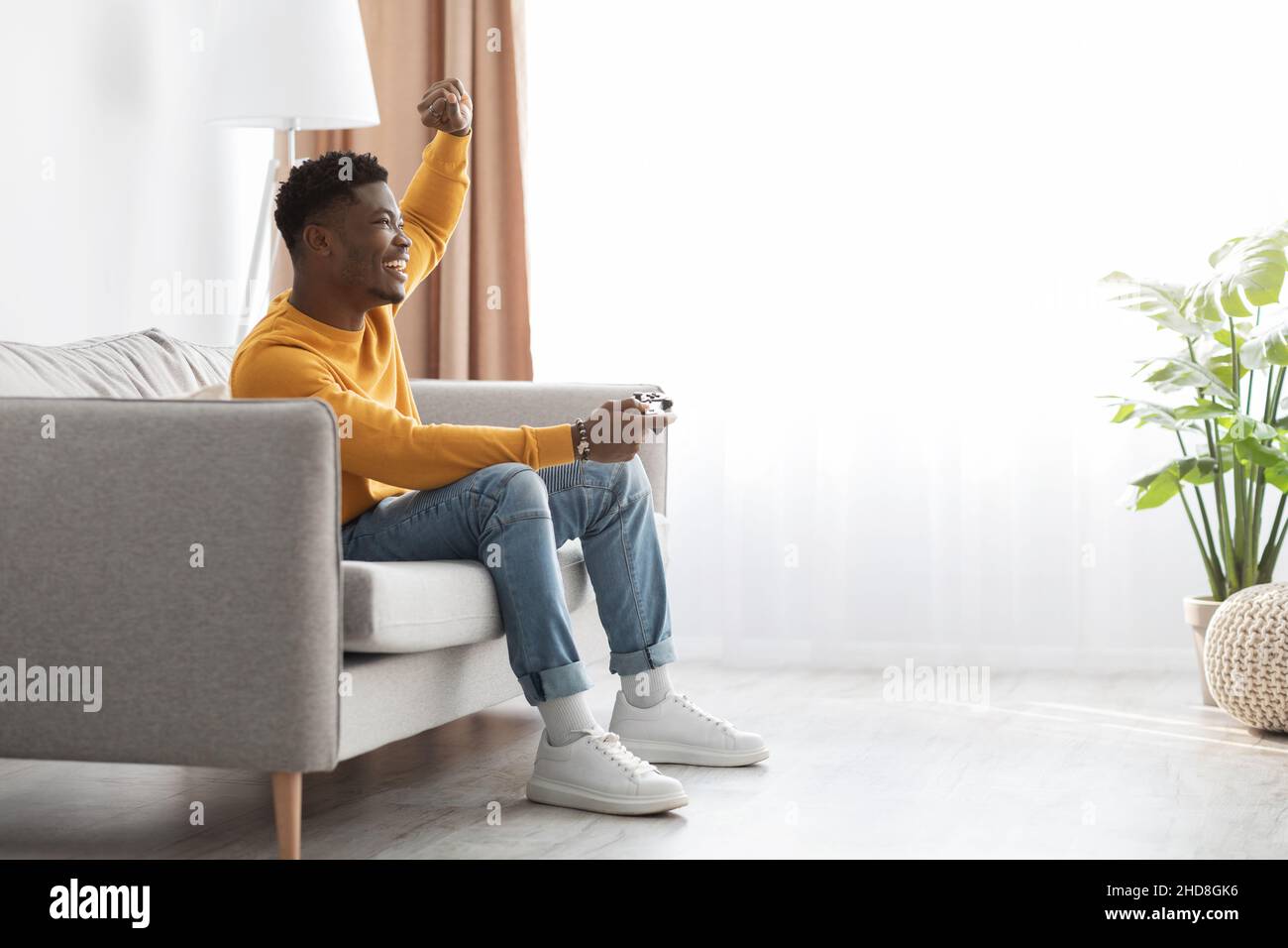 Joyful black guy sitting on couch with joystick Stock Photo