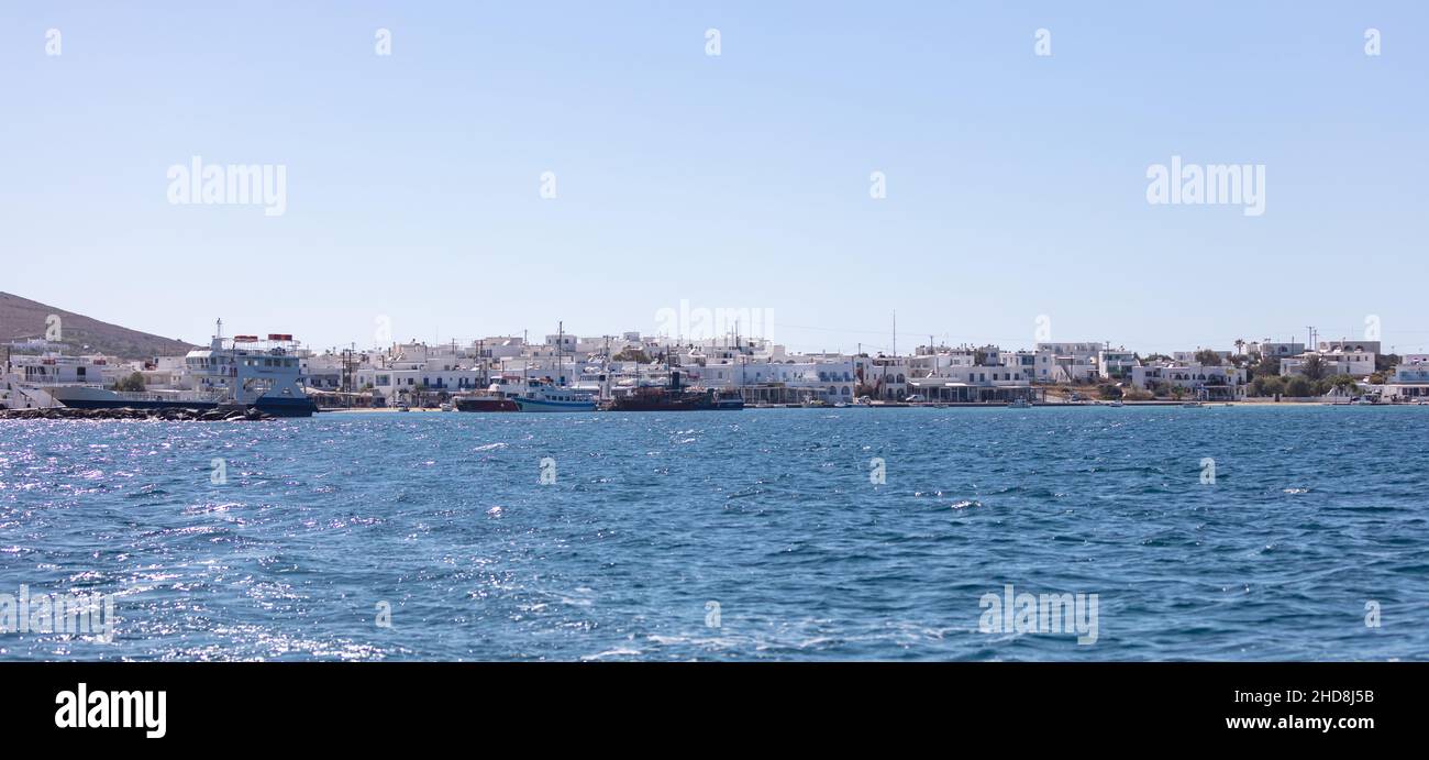 Antiparos island Cyclades Greece. Panoramic view of harbor boats in Aegean sparkle sea whitewashed seaside buildings shops cafe taverns blue sky. Summ Stock Photo