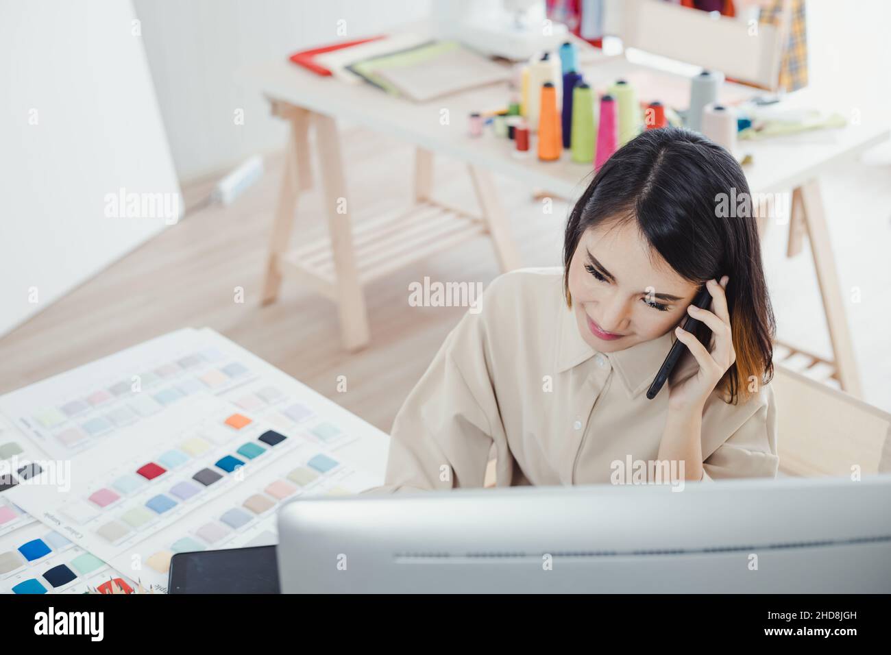 Beautiful Asian woman designer, talking on the phone with the customer and taking note of the work details in order to receive the tailor order for th Stock Photo