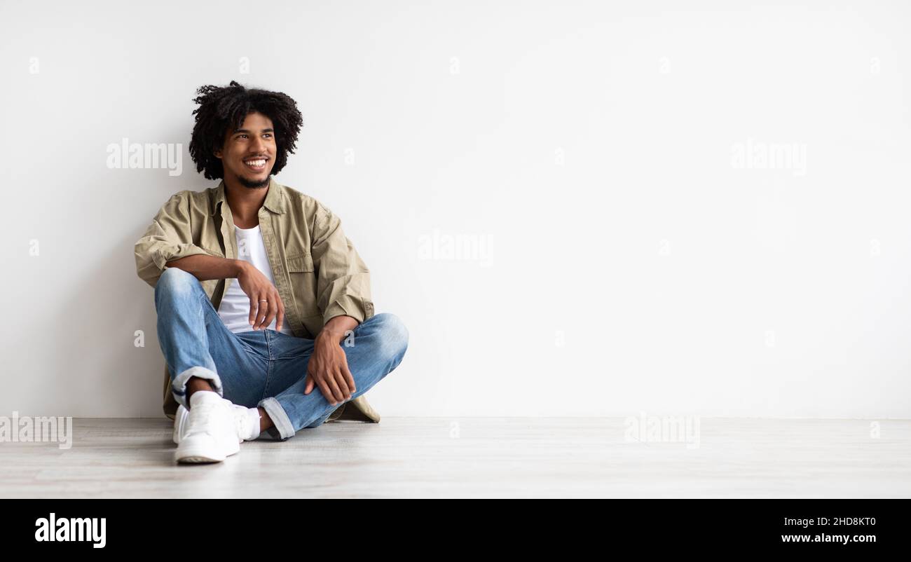 Young Smiling African American Guy Sitting On Floor And Looking Aside Stock Photo