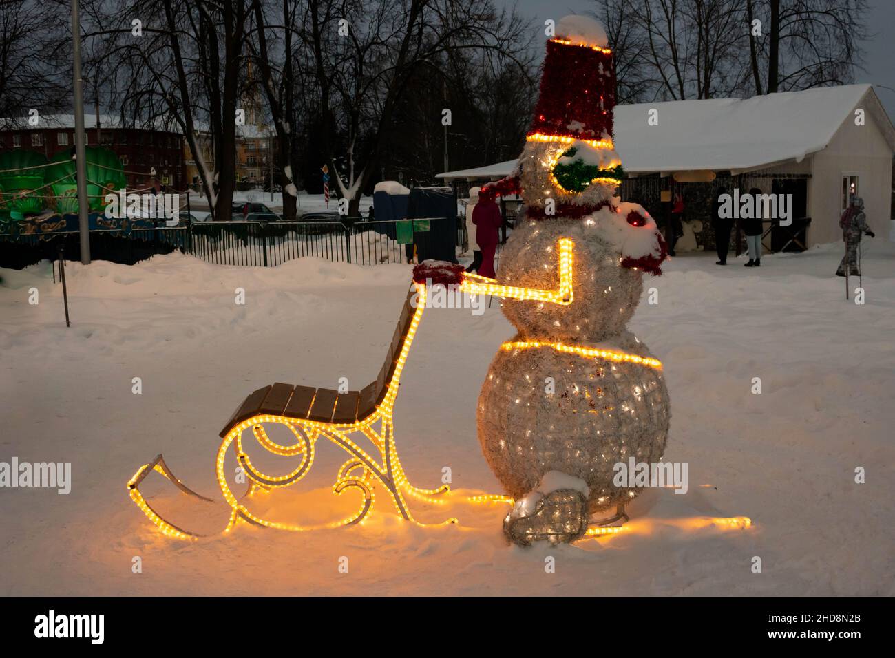 In the evening park, a glowing snowman on a winter sleigh. Stock Photo
