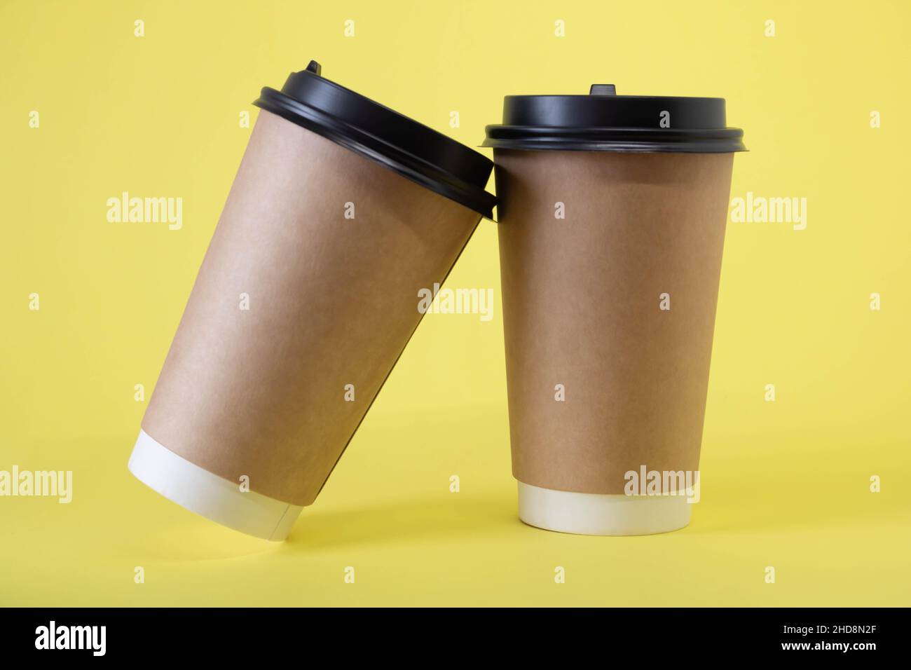 Two brown glasses with lids on a yellow background. Stock Photo