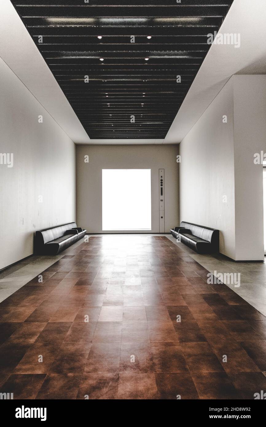 Vertical shot of an empty minimalistic hallway of a building with brown floor tiles and black so Stock Photo