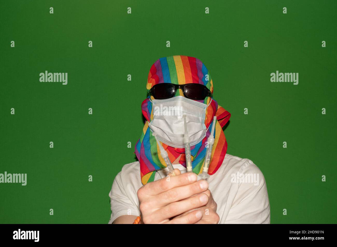 Vaduz, Liechtenstein, December 24, 2021 Person with a medical face mask and a gender rainbow flag is showing some syringes Stock Photo
