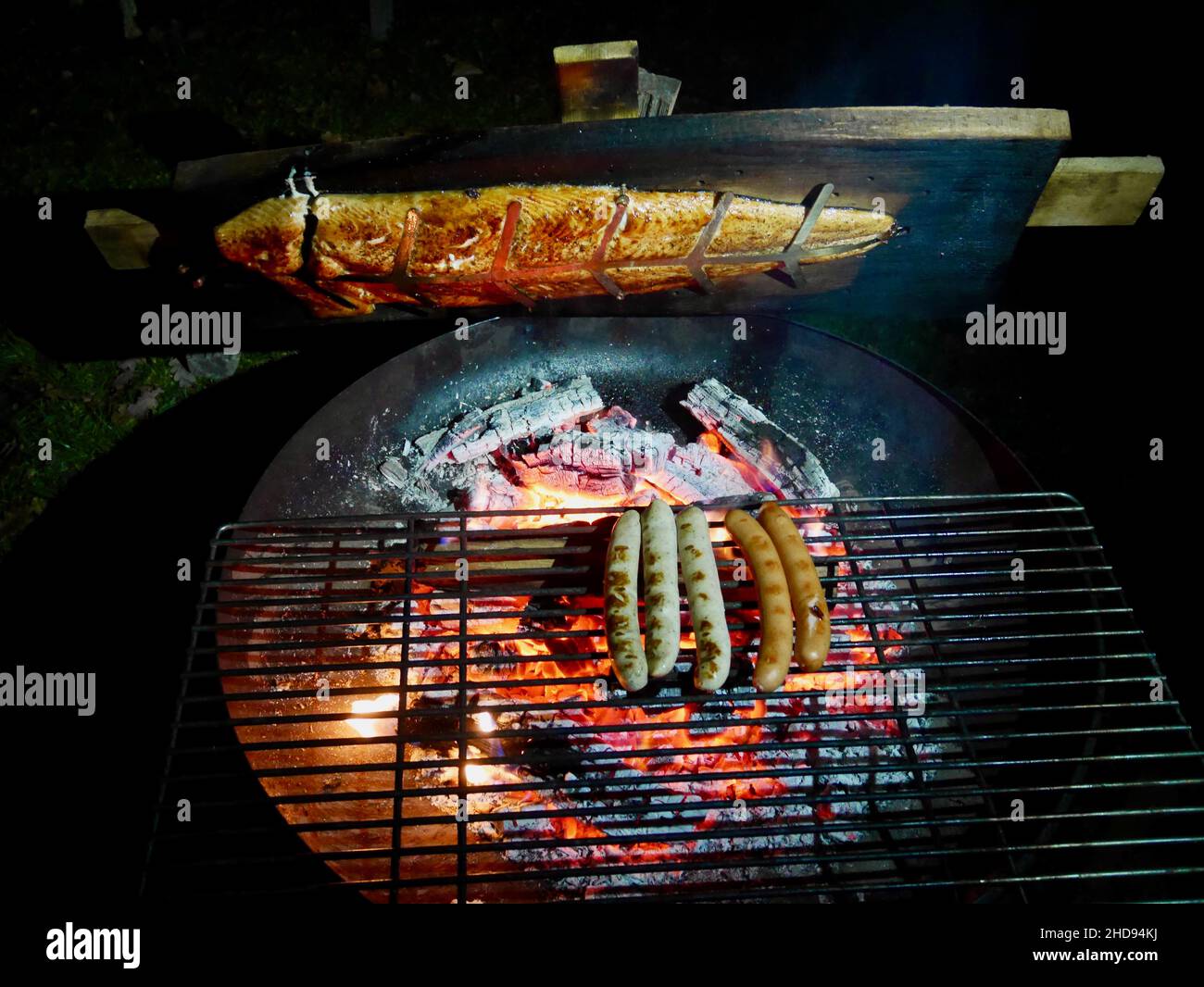 Flame grilled salmon, a traditional Nordic dish, and sausages on fire bowl,  at night. Aerial view Stock Photo - Alamy