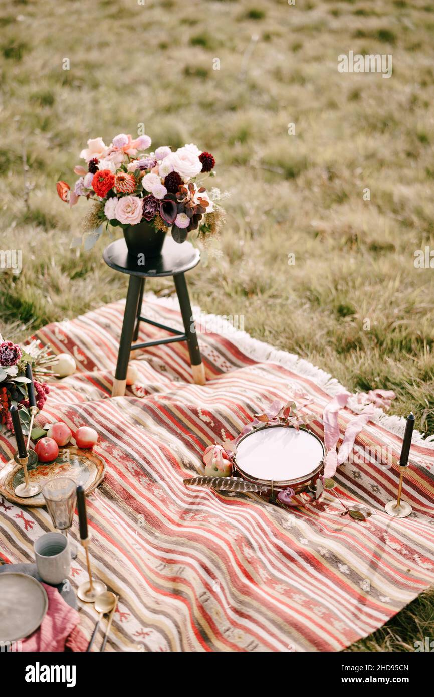 Bouquet of flowers in a flowerpot stands on a small stool on a colorful bedspread in the field Stock Photo