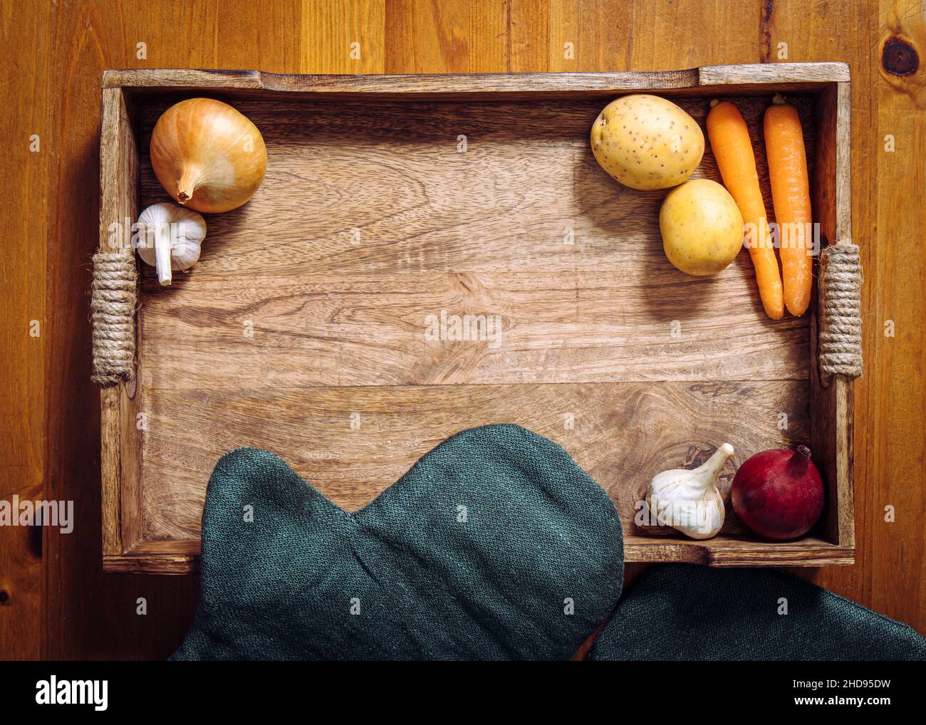 Flat lay view of various root vegetables on wooden tray on kitchen table. Lot of copy space in the center. Carrots, garlic, onion, potatoes. Stock Photo