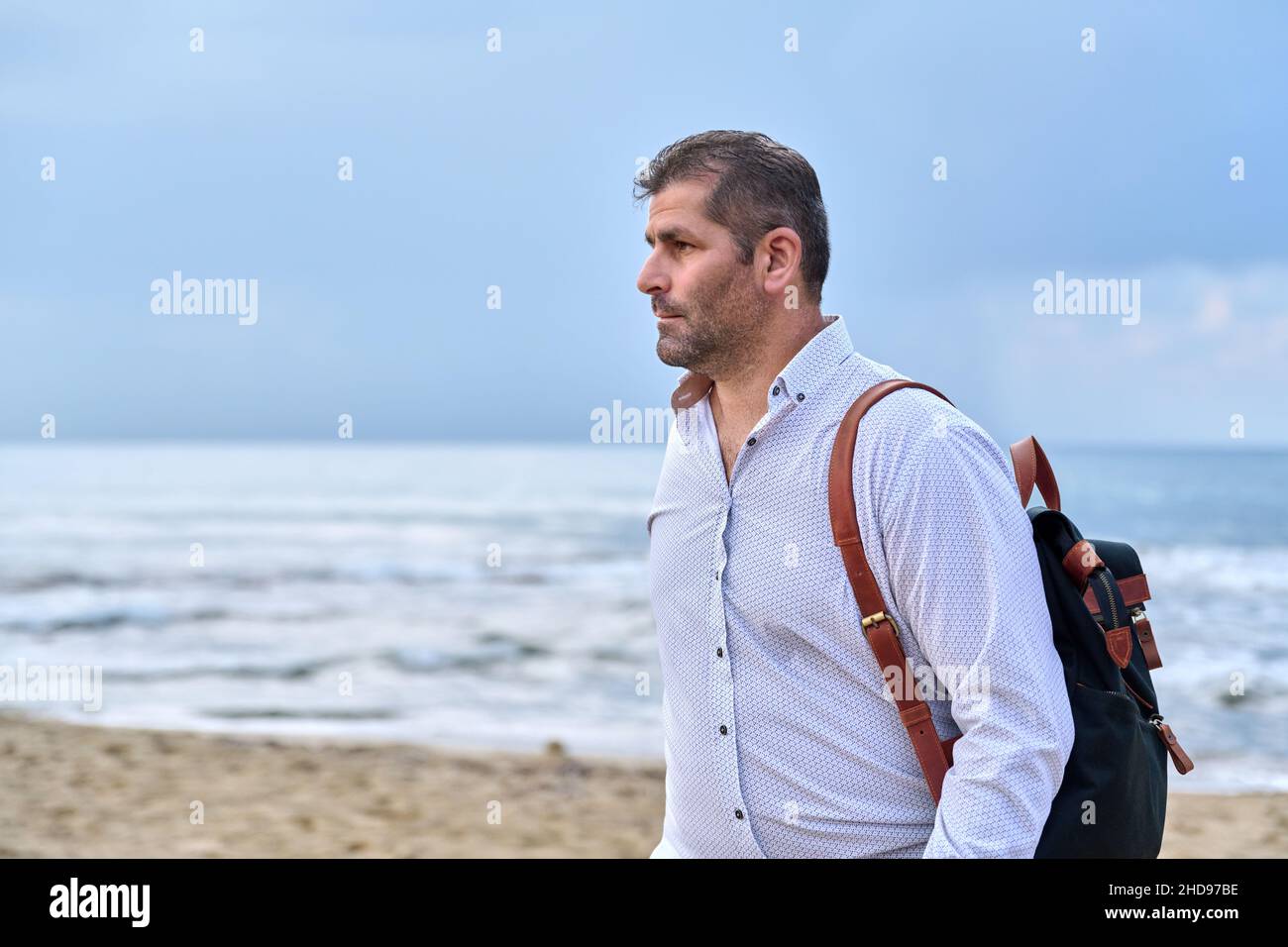 Outdoor portrait of mature man with backpack on seashore, copy space Stock Photo