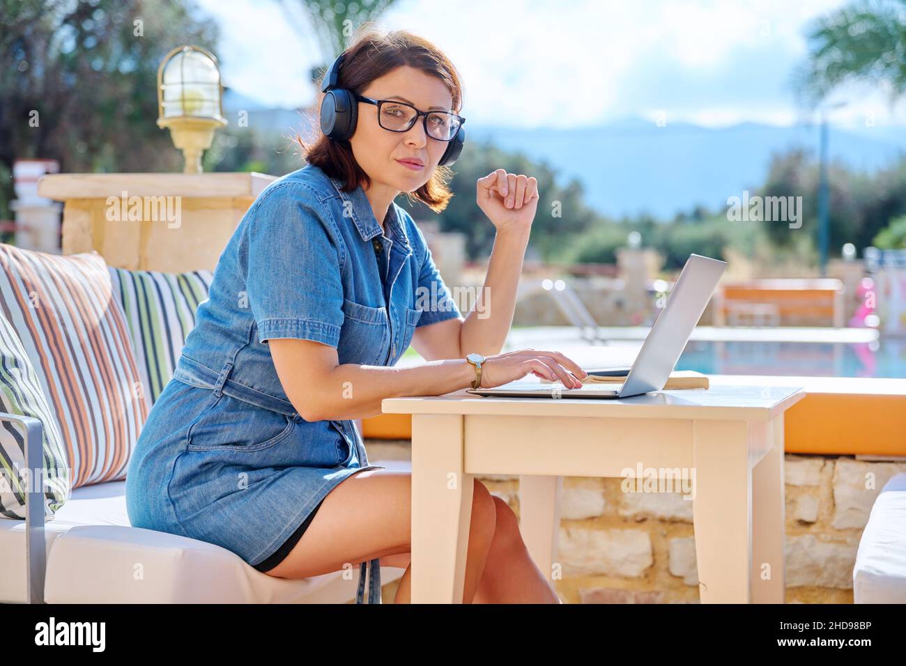 Mature woman working outdoors with headphones using laptop. Stock Photo