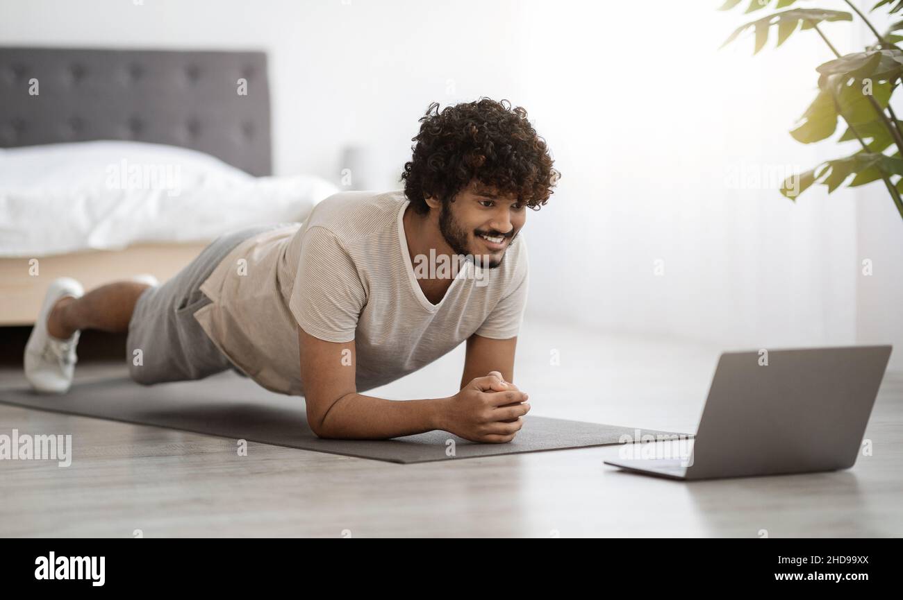Happy athletic hindu man planking at home, using computer Stock Photo