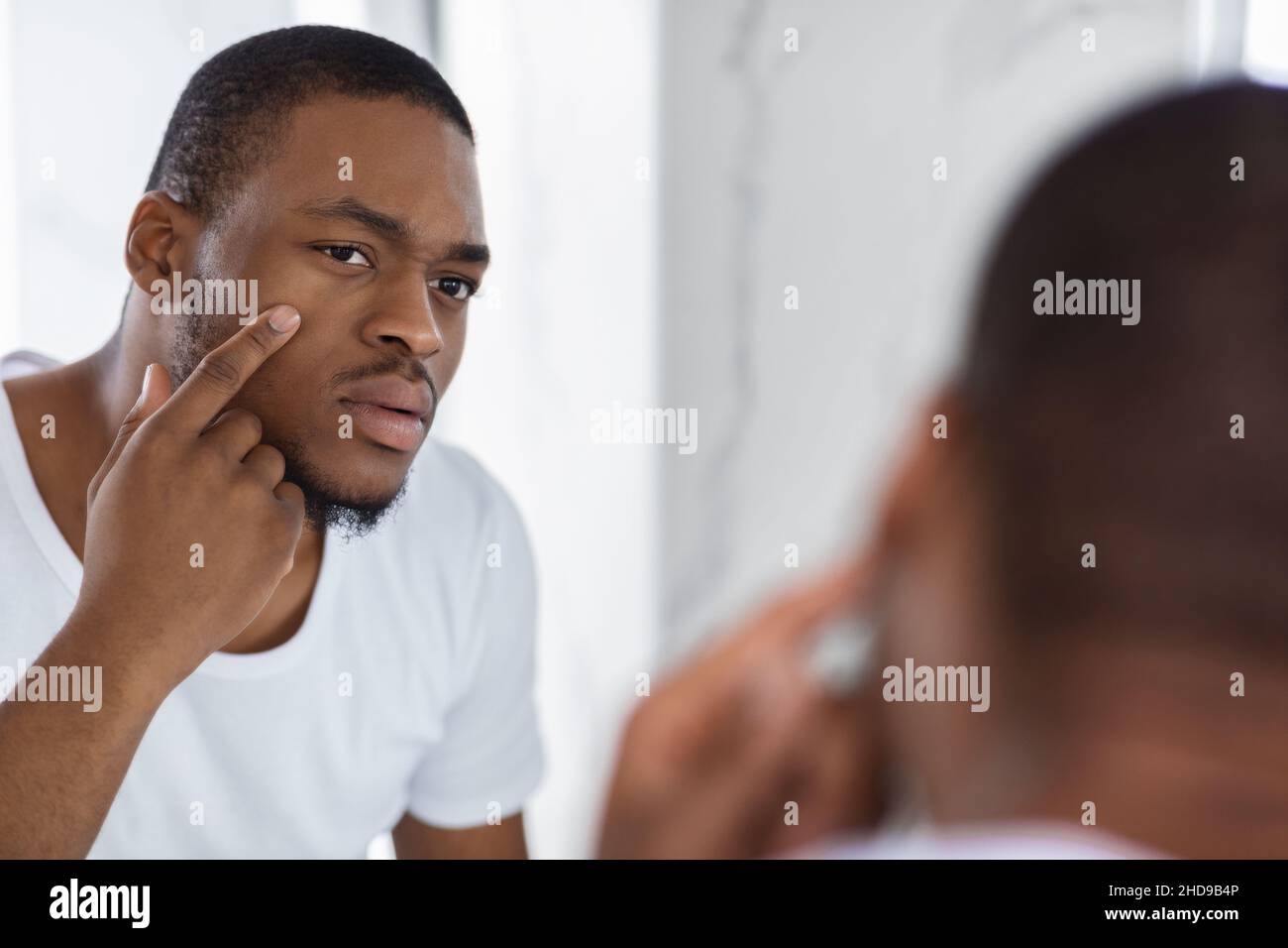 Concerned Black Young Man Examining His Face While Looking At Mirror Stock Photo