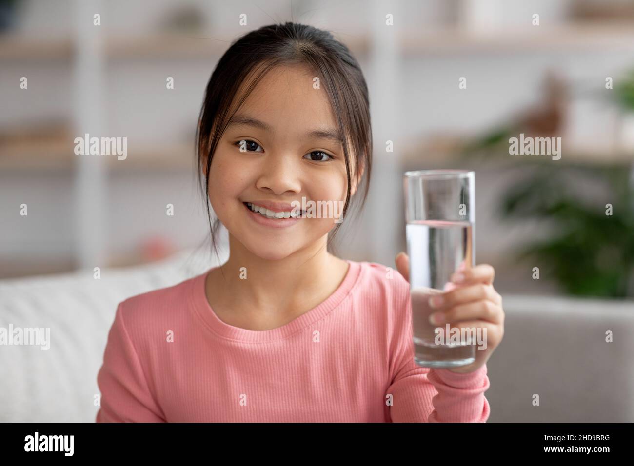 Smiling little girl with glass of water at home Stock Photo - Alamy