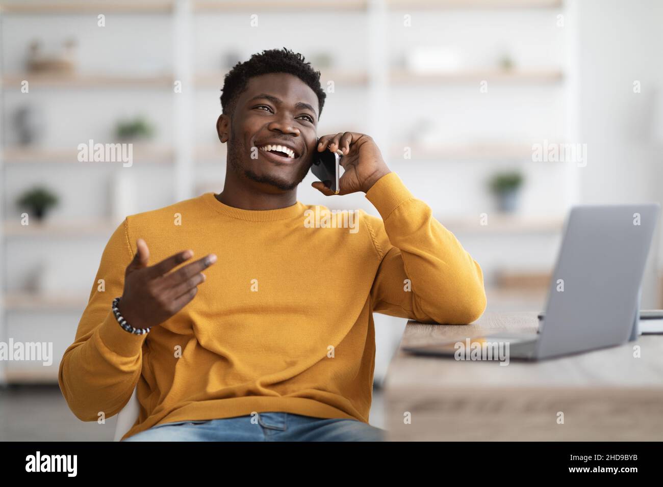 Smiling man sitting at table with laptop, having phone conversation Stock Photo