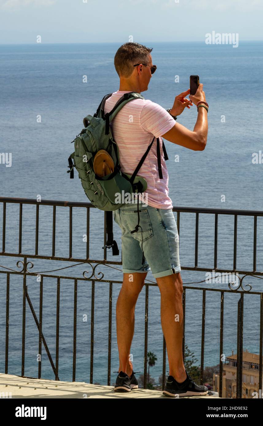 male tourist wearing shorts taking a photograph using a smartphone on