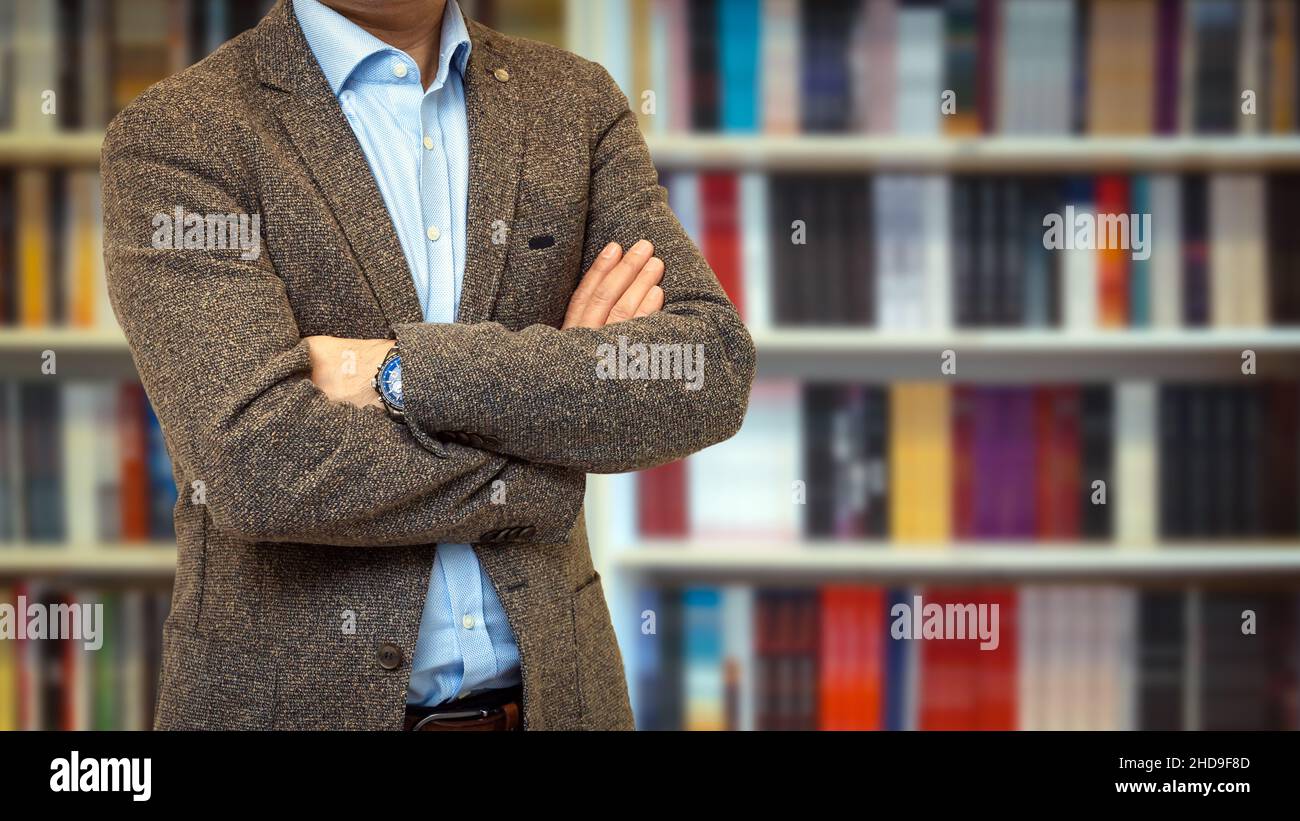 Unrecognizable businessman wearing a suit standing with crossed arms in front of a bookcase Stock Photo