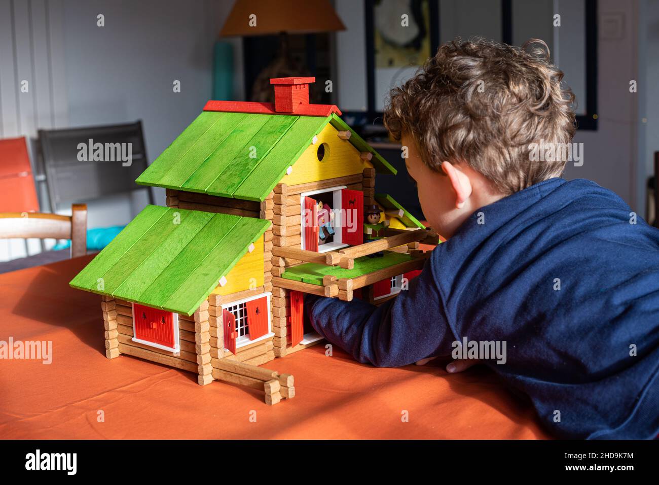Caucasian child boy playing with a vintage wooden log cabin on a table, a creative wood construction toy. Stock Photo