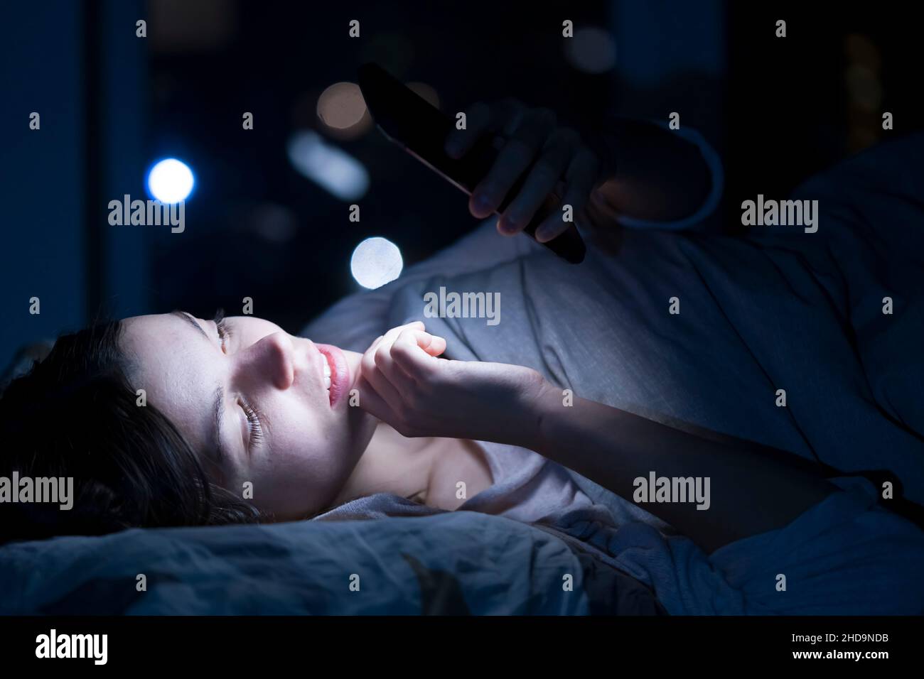 Young girl in a bed with a phone at night. Stock Photo