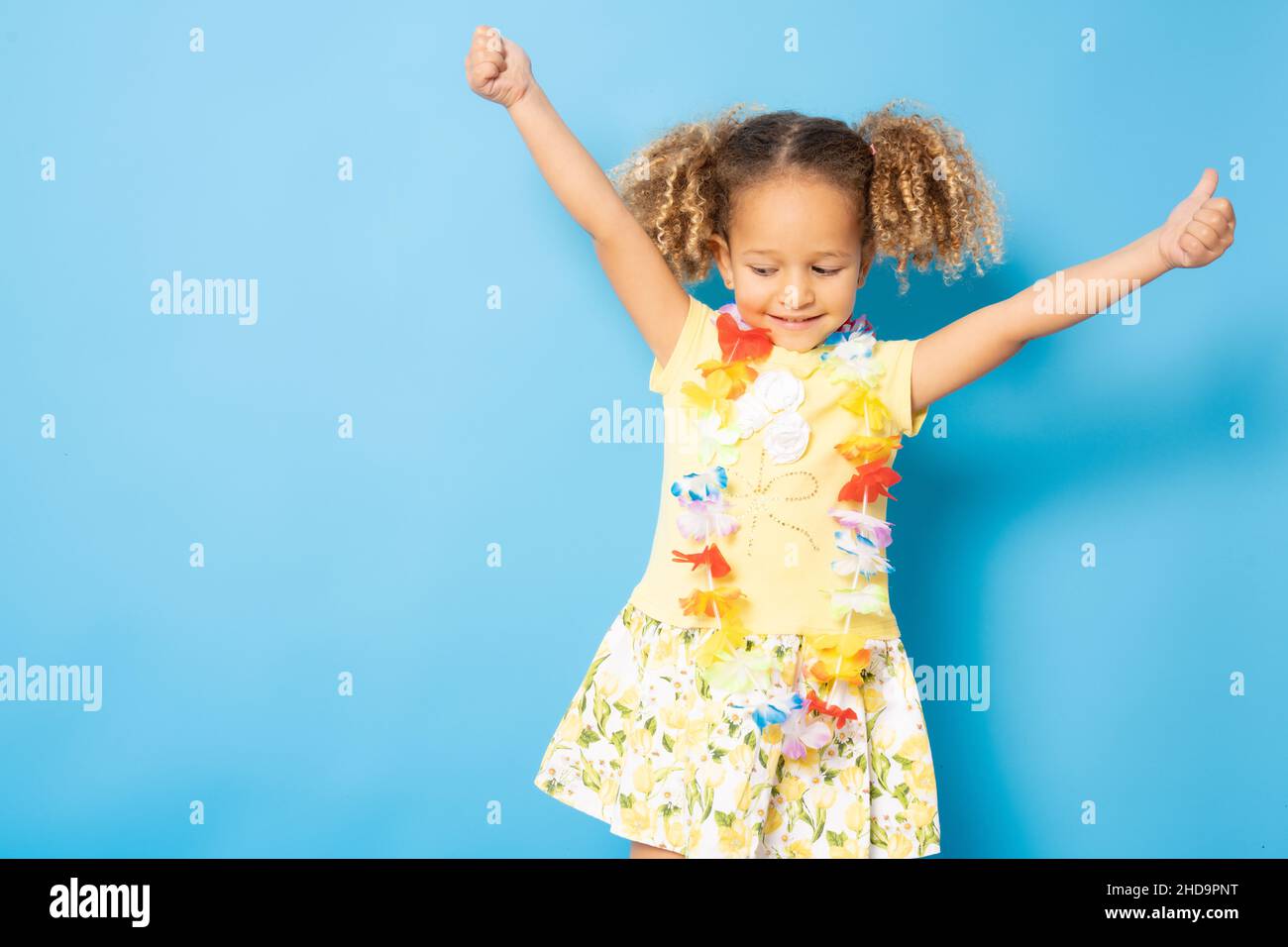 Happy little girl wearing Hawaiian necklace standing isolated over blue background. Stock Photo
