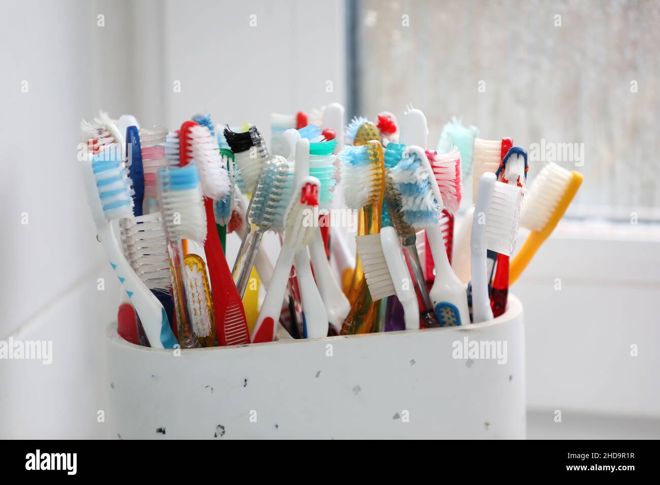 A selection of colourful plastic toothbrushes in a pot in a bathroom in Chichester, West Sussex, UK. Stock Photo