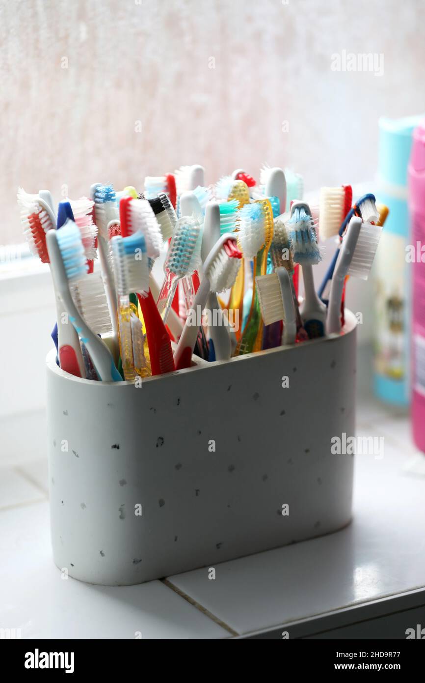A selection of colourful plastic toothbrushes in a pot in a bathroom in Chichester, West Sussex, UK. Stock Photo