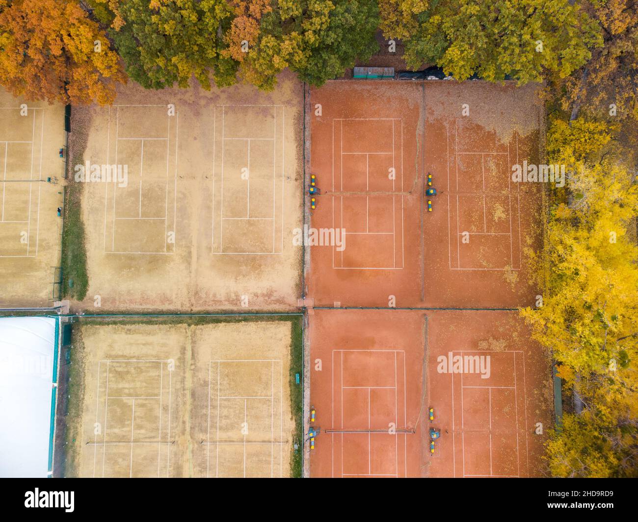 Orange clay tennis courts in city park. Aerial look down on vivid yellow autumn trees near