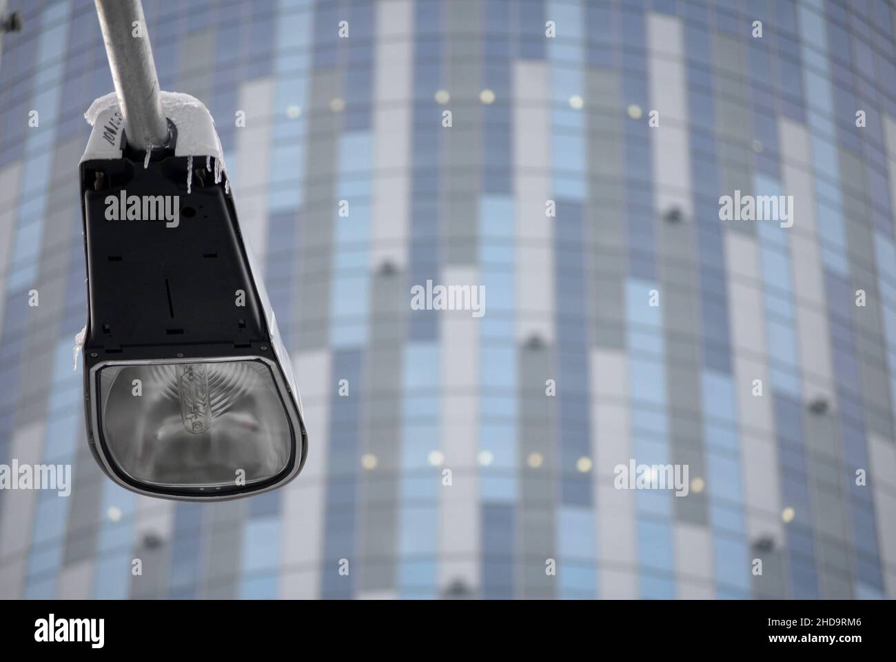 Close up of lamp post with icicles pictured with a modern office building in background. Stock Photo