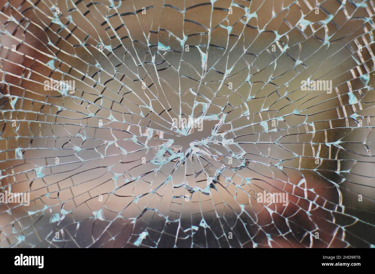 Broken car window with cracked glass pattern and a bullet hole in the middle. Stock Photo