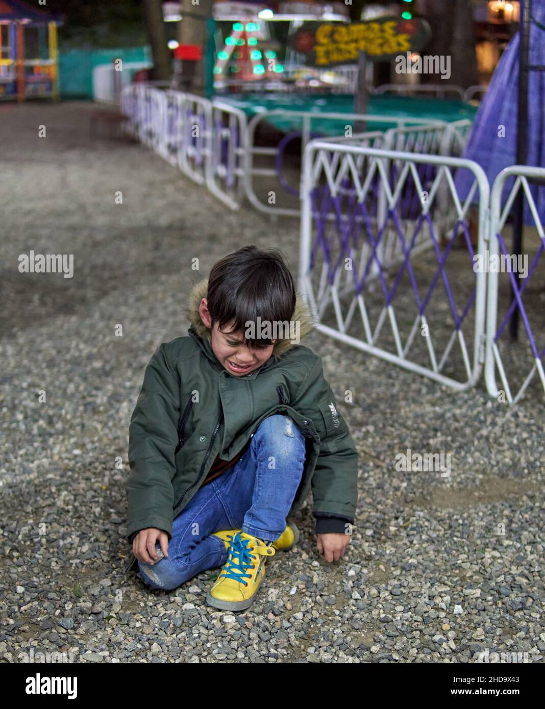 latin little boy looking down and crying in a park, maybe is lost. outdoors, distressed child sitting on pebbles. Argentina Stock Photo